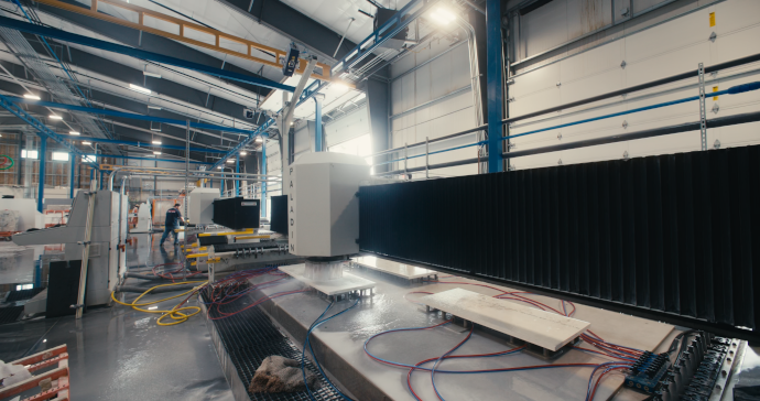 BACA's Paladin 3-axis CNC router in a warehouse. There are several workpieces/slabs of stone on the washdown table.