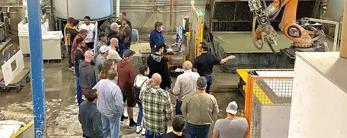 A group of professionals observing a demonstration of robotic technology in a manufacturing facility.